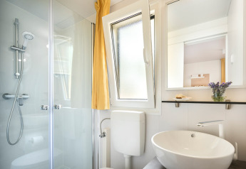 Bagno moderno e luminoso con doccia, lavabo, finestra aperta e specchio al Lopar Garden Home in Croazia.