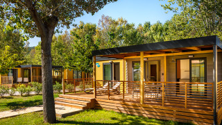 Lodge Lopar Garden Home con porche de madera y rodeado de árboles verdes, ambiente relajante y natural.