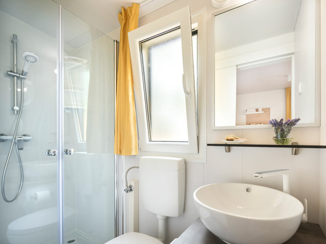 Moderne badkamer met douche, wastafel, spiegel en open raam in Vela Bay Home, Valamar Camping Baška, Kroatië.