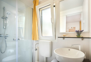 Bagno moderno con doccia, lavabo, specchio e finestra aperta al Vela Bay Home, Valamar Camping Baška, Croazia.