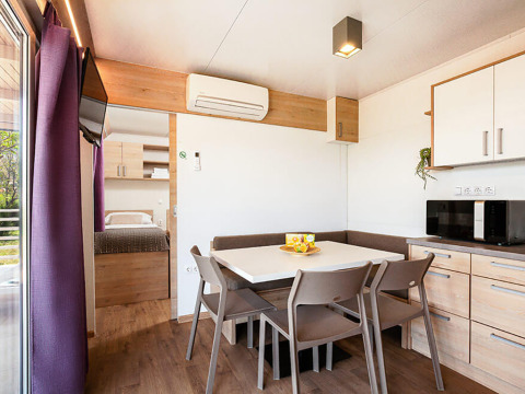 Interior de la cabaña Sunny Beach Home en Valamar Camping Baška, Croacia, con mesa de comedor y cocina.