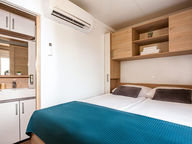 Chambre moderne du Sunny Beach Home à Valamar Camping Baška, Croatie, avec lit double et rangements en bois.