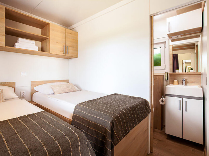 Bright twin bedroom with cozy decor, wooden cabinets and private bathroom at Sunny Beach Home in Croatia.