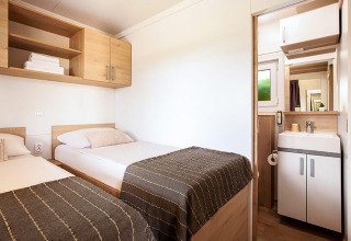 Habitación luminosa con dos camas individuales, armarios de madera y baño privado en Sunny Beach Home, Croacia.