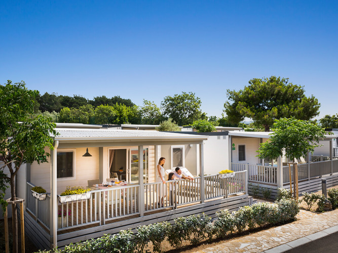 Famiglia si rilassa sulla veranda del lodge Krk Home al Valamar Camping Krk in Croazia, giornata soleggiata.