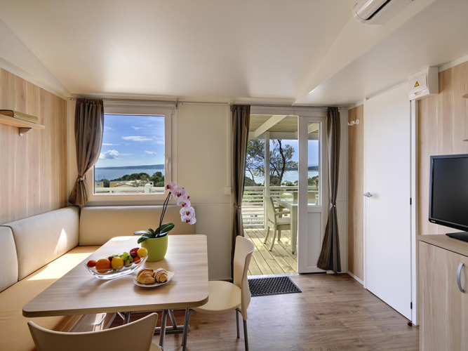 Moderne lodge woonkamer met eettafel, fruit en zeezicht vanop het terras bij Valamar Camping Krk, Kroatië.