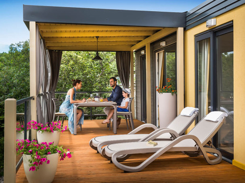 Gezin geniet van ontbijt op het terras van Bella Vista Home lodge, met zicht op bomen en bloemen.