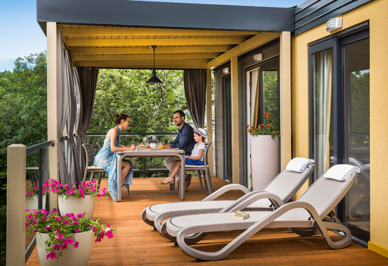 Gezin geniet van ontbijt op het terras van Bella Vista Home lodge, met zicht op bomen en bloemen.