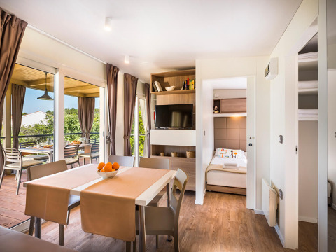Moderne lodge met eethoek, open slaapkamer, balkon, grote ramen en bruin gekleurde gordijnen.