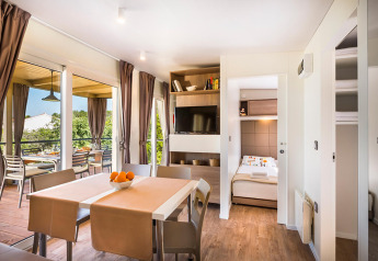 Moderne lodge med spisestue, opholdsområde, åbent soveværelse, balkon og store vinduer med gardiner.