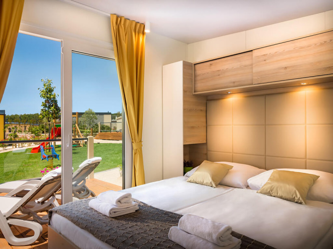 Dormitorio en Bella Vista Home, Valamar Camping Krk, Croacia, con acceso a terraza y vista al área de juegos.