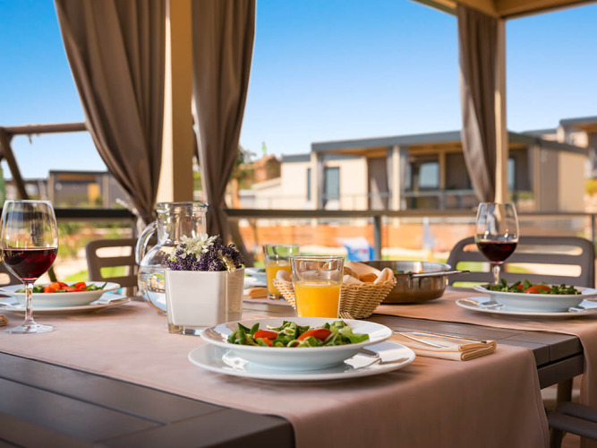 Udendørs spisebord ved Bella Vista Home på Valamar Camping Krk, Kroatien, dækket med salater og vin.