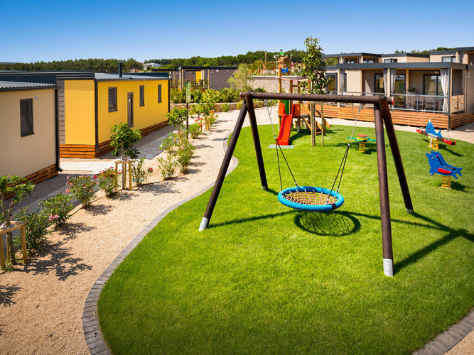 Speeltuin met schommel en glijbaan bij Bella Vista Home op Valamar Camping Krk in Kroatië, omringd door lodges.