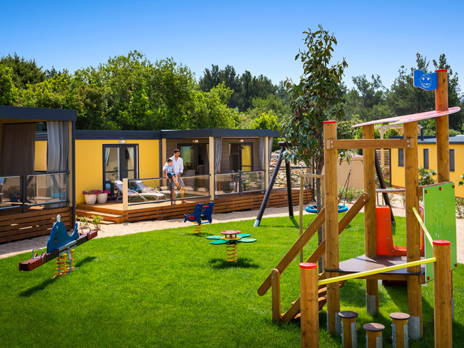 Speelplein en lodges met terras bij Bella Vista Home, Valamar Camping Krk in Kroatië, zonnige dag, groen gras.