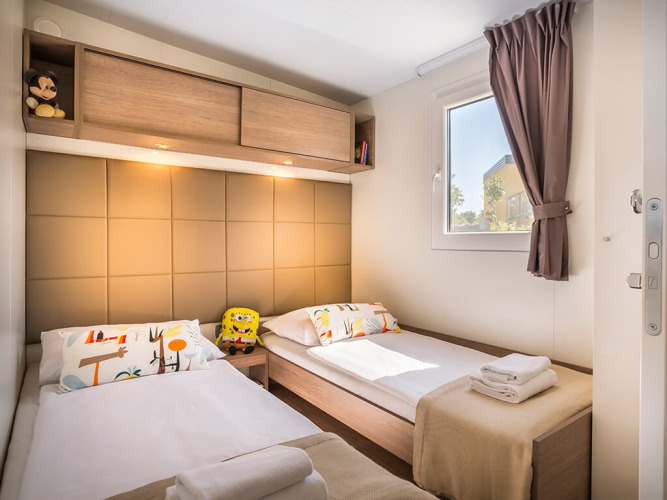 Modern twin bedroom in Bella Vista Home with plush toys, window, and cozy lighting at Valamar Camping Krk