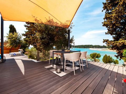 Deck with dining table under shade sail overlooking the sea at Family Holiday Home Pool, Camping Porton Nature Hideouts.