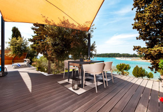 Terraza con mesa para comer bajo toldo, vista al mar en Family Holiday Home Pool, Camping Porton Nature Hideouts, Croacia.
