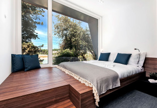 Dormitorio moderno con gran ventanal panorámico, muebles de madera y vistas a la naturaleza en Camping Porton, Croacia.