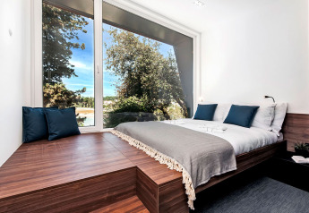 Dormitorio moderno con gran ventanal panorámico, muebles de madera y vistas a la naturaleza en Camping Porton, Croacia.