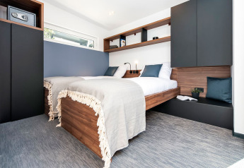 Dormitorio moderno con dos camas de madera, cojines azules y blancos, y diseño minimalista en una casa familiar.