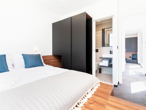 Moderne slaapkamer met dubbel bed, blauwe kussens, zwarte kast en ensuite badkamer in Kroatische lodge.