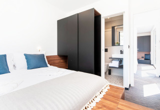 Moderne slaapkamer met dubbel bed, blauwe kussens, zwarte kast en ensuite badkamer in Kroatische lodge.