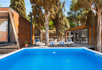 Outdoor pool and modern lodges surrounded by trees at Couple Holiday Home Pool, Camping Porton Nature Hideouts, Croatia.