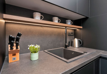 Rincón de cocina moderno con encimera gris, fregadero, cuchillos y tazas en lodge vacacional en Croacia.