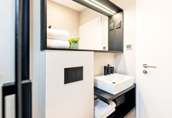 Baño moderno y compacto con lavabo cuadrado, toallas, espejo y planta en Camping Porton Nature Hideouts, Croacia.