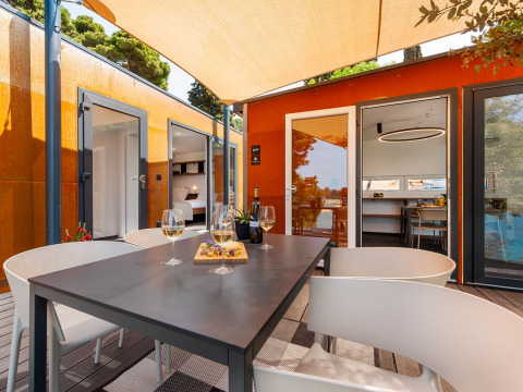 Terrasse des Family Holiday Home Pool bei Camping Porton Nature Hideouts in Kroatien mit Tisch, Wein und Snacks.