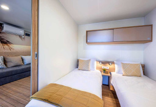 Modern lodge bedroom with two single beds and adjoining lounge area at Camping Porton, Croatia.