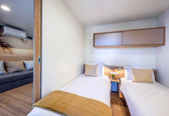 Moderne lodge-soveværelse med to enkeltsenge og tilstødende opholdsområde i Camping Porton, Kroatien.