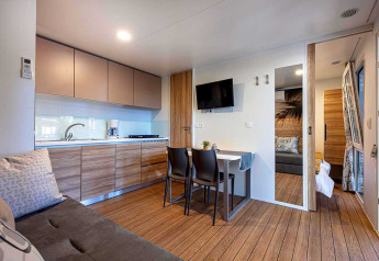 Interno lodge moderno con cucina, tavolo da pranzo, divano e camera da letto a Camping Porton, Croazia.