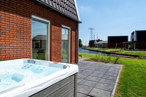 Bubbelbad op terras met uitzicht op gracht en moderne huizen in vakantiepark Tusken de Marren, Friesland.