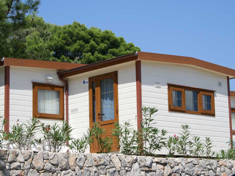Lodge Baia Lux à Baia Holiday Poljana en Croatie, maison blanche avec charpente bois et muret de pierre devant.