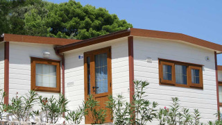 Lodge Baia Lux al Baia Holiday Poljana in Croazia, casa bianca con rifiniture in legno e muro in pietra davanti.