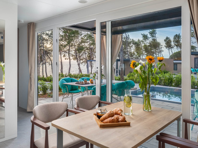 Tavolo da pranzo con croissant e girasoli, vista sulla piscina e sul mare all'Aminess Style Camping Avalona Resort, Croazia.