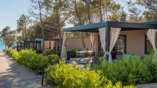 Premium Holiday Home Chalet mit überdachter Terrasse, Gartenmöbeln und üppigem Grün am Meer.