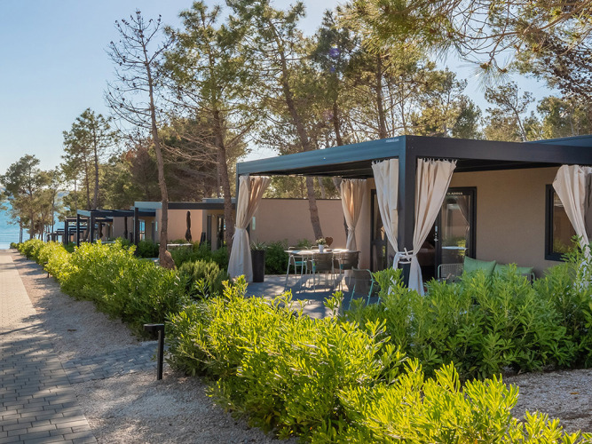 Chalet Premium Holiday Home con terrazza privata e tende, immerso nel verde vicino al mare.