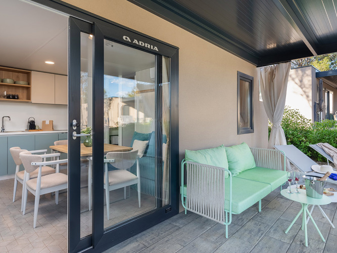 Terrazza esterna con divano e tavolo davanti a una cucina moderna al Premium Holiday Home, Aminess Style Camping Avalona Resort, Croazia.