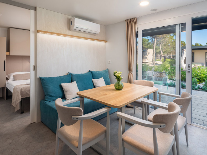 Soggiorno moderno con tavolo da pranzo e divano blu nel Premium Holiday Home di Aminess Style Camping Avalona Resort, Croazia.