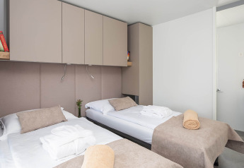 Chalet moderno con due letti singoli, biancheria beige e armadi all'Aminess Style Camping Avalona Resort.