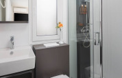 Bagno moderno con doccia in vetro, lavabo quadrato, finestra opaca e fiore giallo all’Aminess Style Camping Avalona Resort.