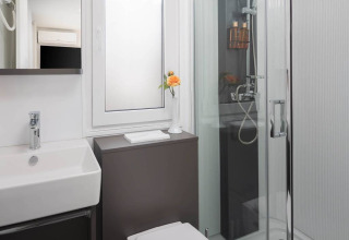 Baño moderno con ducha de cristal, lavabo cuadrado, ventana esmerilada y flor amarilla en Avalona Resort, Croacia.
