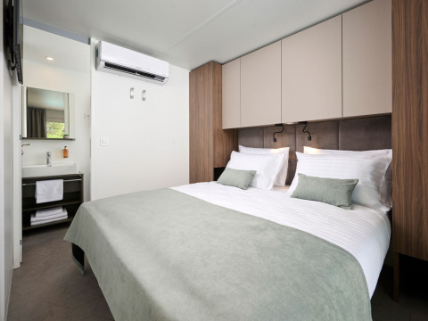 Moderne slaapkamer met tweepersoonsbed, groene kussens en badkamer in Amber Luxury Holiday Home, Aminess Style Camping Atea Resort, Kroatië.