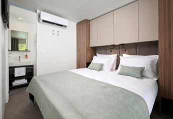 Moderne soveværelse med dobbeltseng, grønne puder og badeværelse på Amber Luxury Holiday Home, Aminess Style Camping Atea Resort, Kroatien.