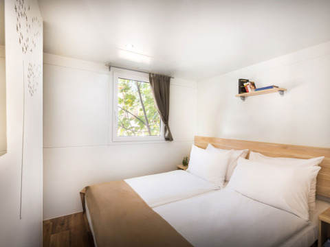 Dormitorio luminoso con cama doble, ventana y estante en Comfort Holiday home, Aminess Style Camping Atea Resort, Croacia.