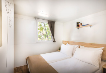 Soveværelse med dobbeltseng, lyse vægge, vindue med gardin og en hylde, Comfort Holiday home, Kroatien.