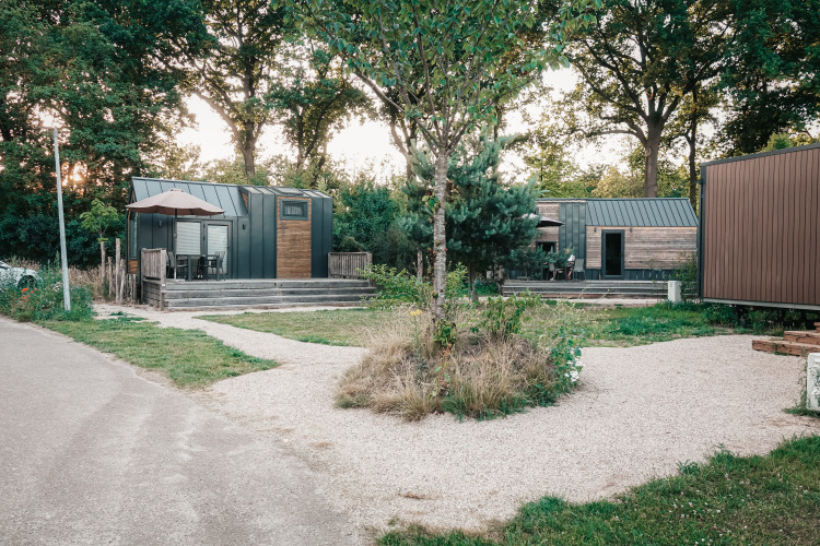 Casas diminutas modernas rodeadas de árboles y senderos de grava, foto tomada en Tiny House al atardecer.