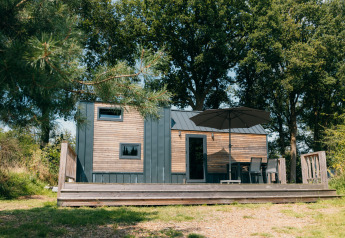 Petite maison en bois avec terrasse et parasol, entourée d'arbres à Holiday Park Sallandshoeve, Pays-Bas.